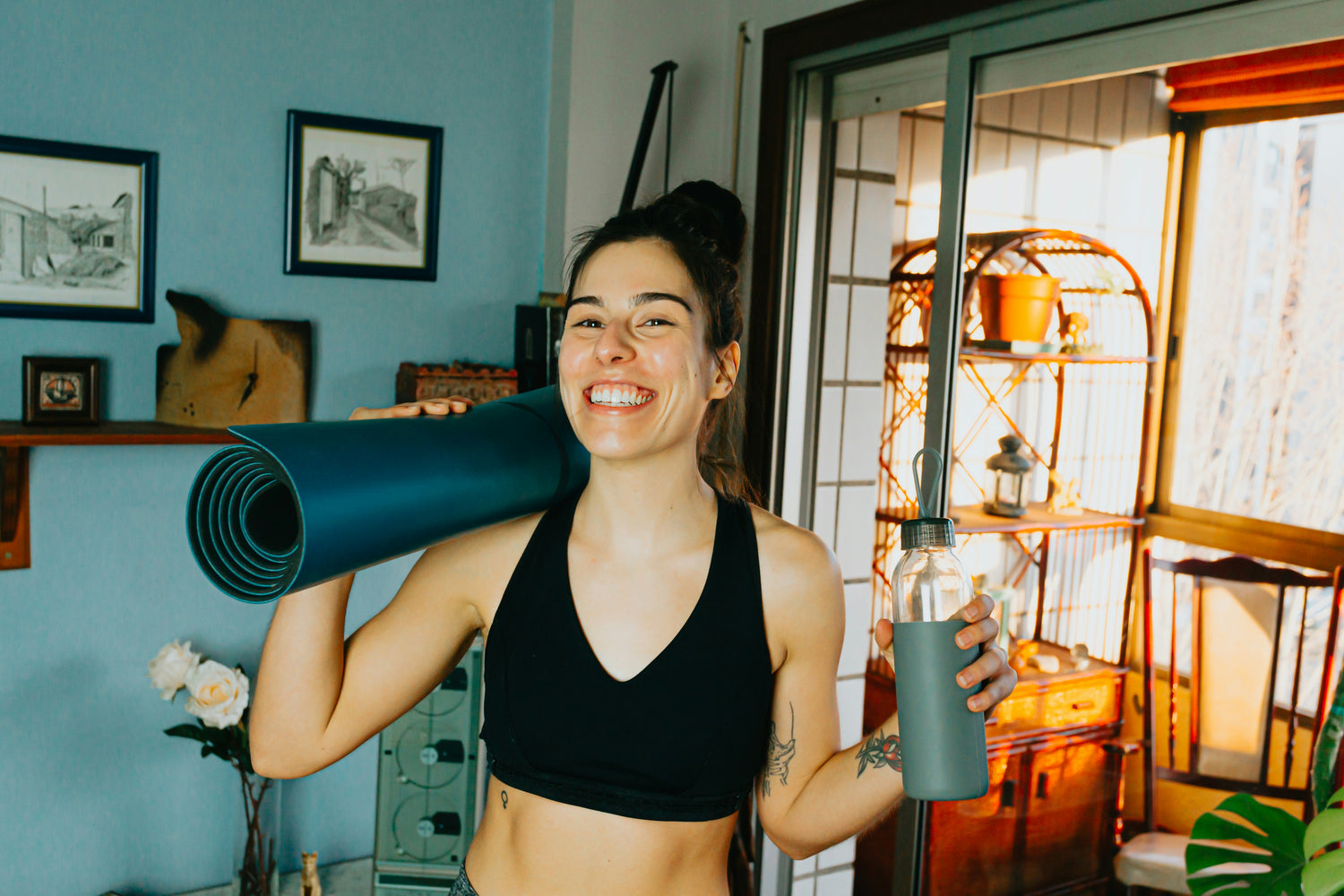 Happy woman after home workout holding a yoga mat and water bottle, representing Unchecked Fitness users who track protein, macros, and hydration for optimized wellness goals.